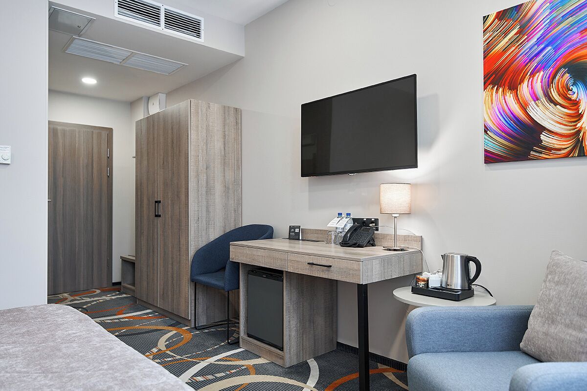 Habitación de hotel con escritorio, silla y cama. Hay un televisor montado en la pared y un cuadro sobre el escritorio.