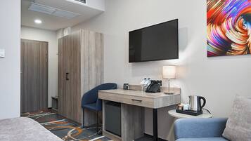 Habitación de hotel con escritorio, silla y cama. Hay un televisor montado en la pared y un cuadro sobre el escritorio.