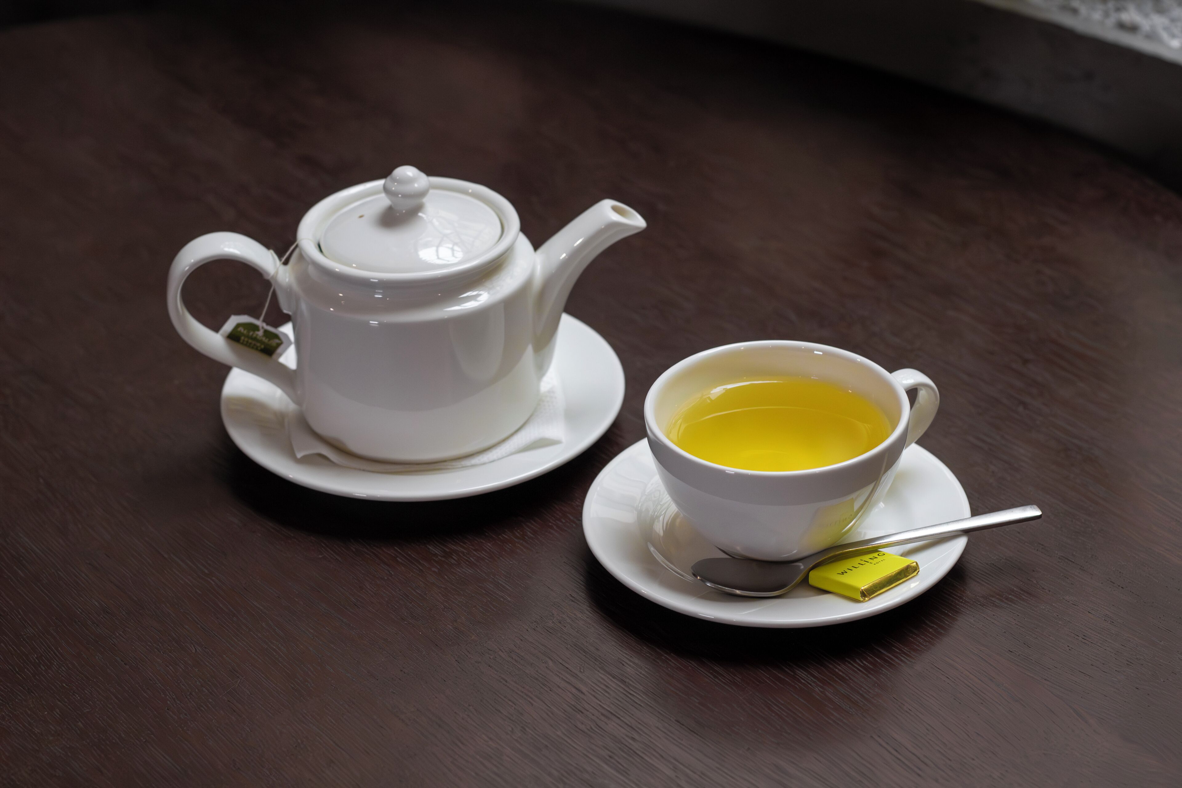 A white teapot and cup on a wooden table.