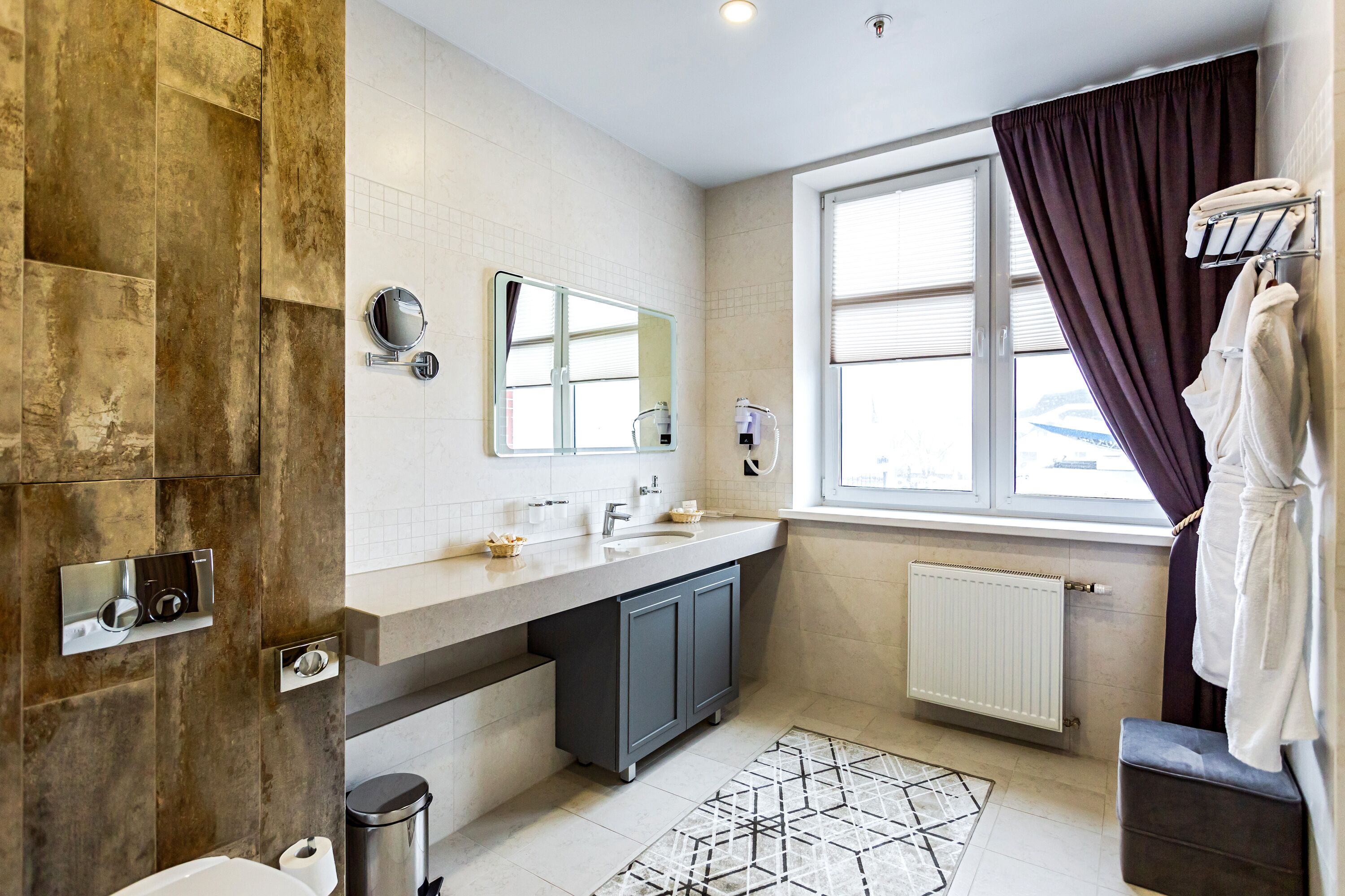 A modern bathroom with a large mirror, a sink, a toilet, and a window with curtains.