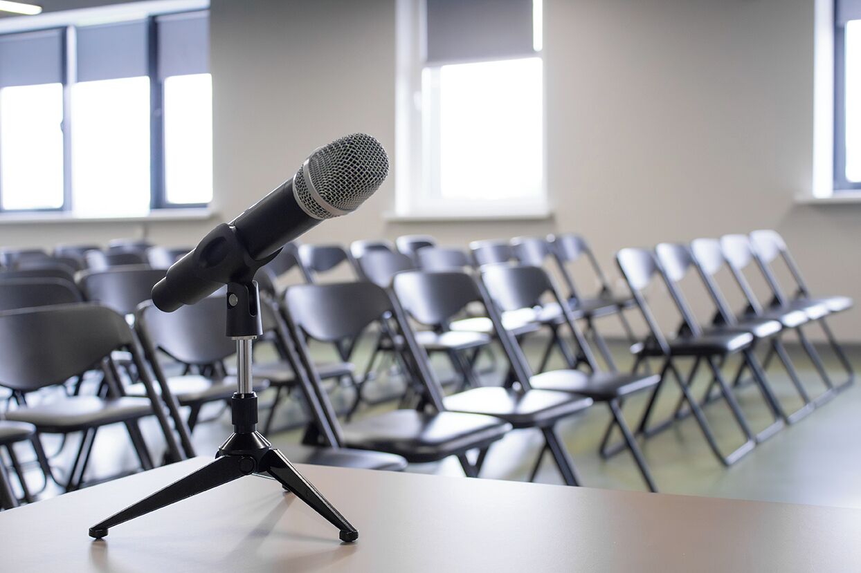 A conference room with rows of chairs and a microphone on a stand.