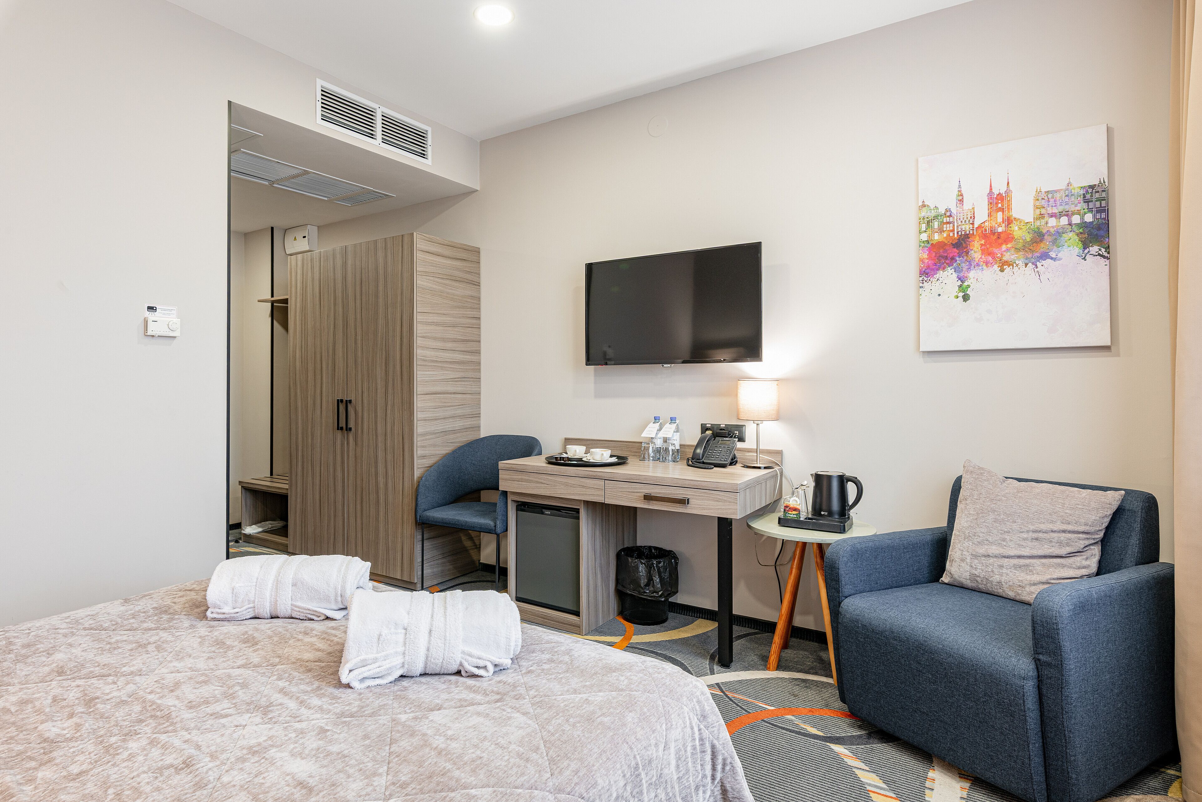 Een hotelkamer met een bed, een bureau, een stoel, een televisie en een schilderij aan de muur.