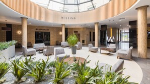 Een moderne hotel lobby met een centraal zitgedeelte, een bord van het restaurant en een glazen dak.