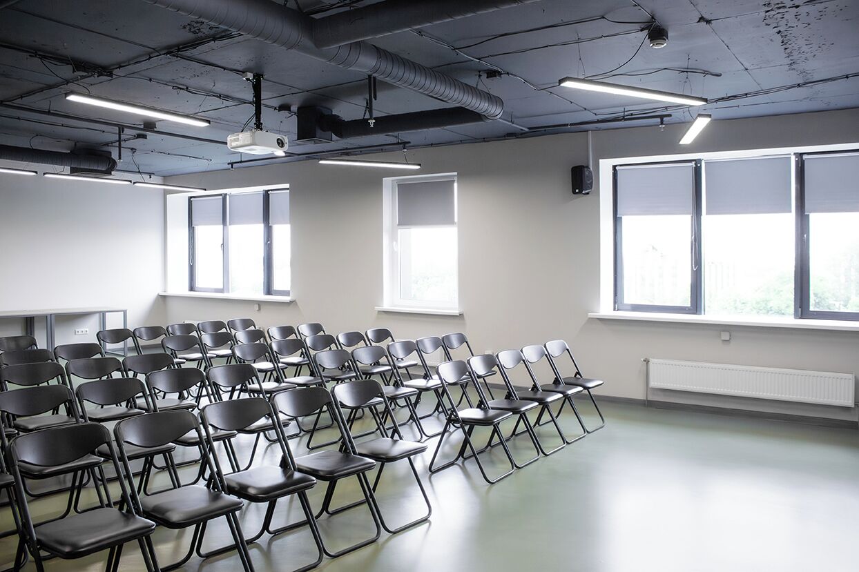 Ein Konferenzraum mit Reihen von Stühlen, großen Fenstern und einem Projektor an der Decke.