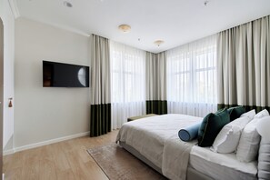 Un dormitorio con cama, televisor de pantalla plana montado en la pared y ventana con cortinas translúcidas.