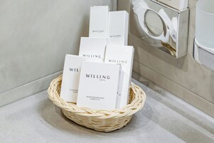 Una cesta de mimbre con varias cajas blancas etiquetadas como “WILLING HOTEL” sobre una encimera de baño.