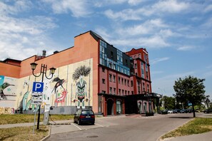 A hotel with a mural on the side, a parking sign, and a car parked in front. - Willing Hotel (Minsk)