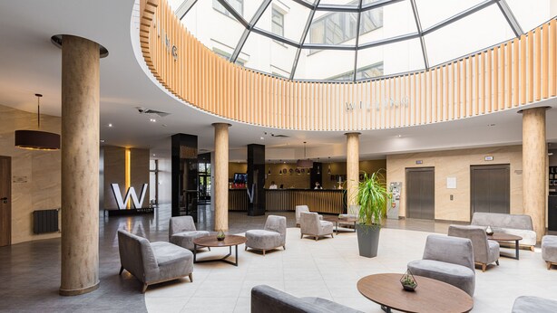 Een ruime lobby met een centraal atrium, zitgedeeltes en een receptiebalie.