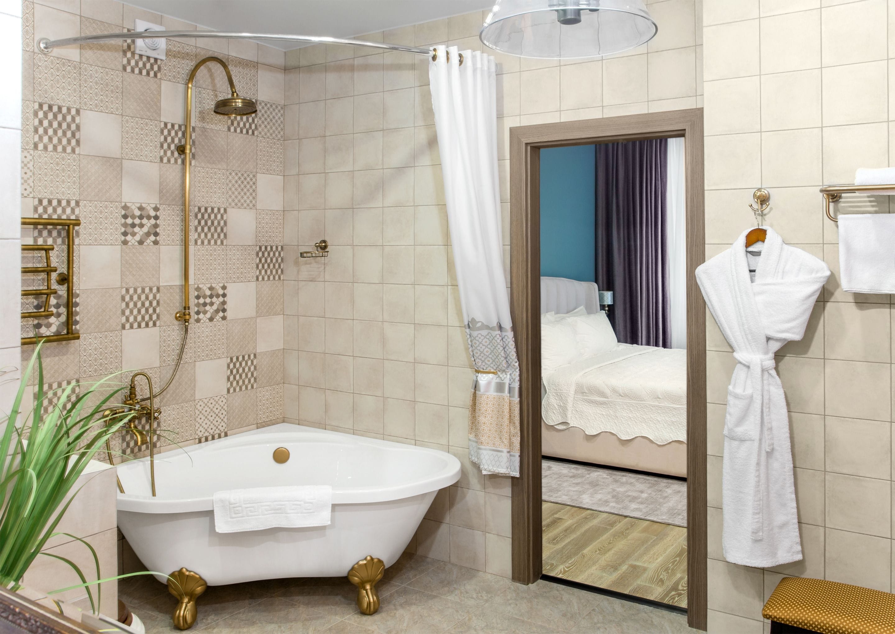 A bathroom with a freestanding bathtub, a shower with a glass door, a mirror reflecting a bed, and a robe hanging on a hook.