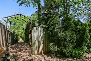 Escape to a serene natural oasis beneath a shaded pergola surrounded by lush greenery and a tranquil wooded environment.