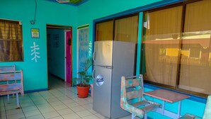 Habitació amb nevera, una cadira, taula petita i una planta en test.