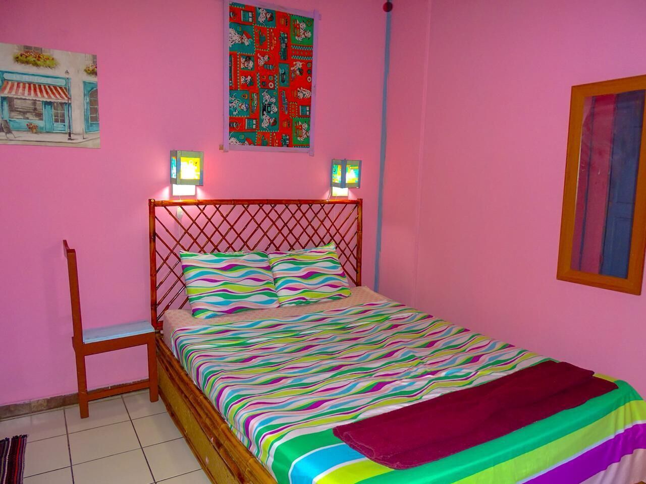 Ein Schlafzimmer mit einem Bettgestell aus Holz, einer farbenfrohen, gestreiften Bettdecke und einem Stuhl.