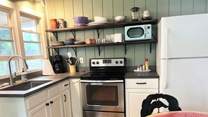 A kitchen with white cabinets, a stainless steel stove, a microwave, and a refrigerator. There is a wooden floor and a large watermelon on the table.