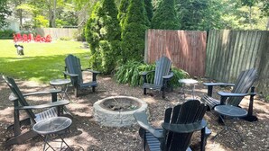 A backyard with Adirondack chairs, a fire pit, and a wooden fence.