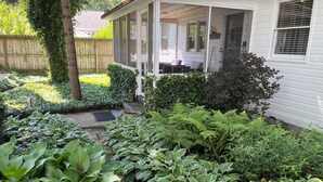 A house with a covered porch, a wooden fence, and various green plants.