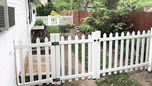 A white picket fence in a backyard with a wooden deck, a table, and chairs. - 1 bed/1 bath, 1.5 blocks to beach/town, dog friendly, fenced yard (Union Pier)