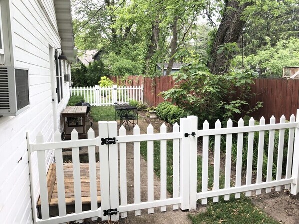 A white picket fence in a backyard with a wooden deck, a table, and chairs.