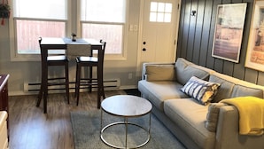A living room with a sofa, a round coffee table, a dining table with chairs, and a door with a window. - 1 bed/1 bath, 1.5 blocks to beach/town, dog friendly, fenced yard (Union Pier)
