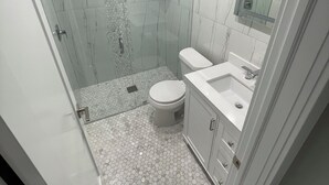 Un bagno moderno con cabina doccia in vetro, un water e un lavabo con specchio sopra.