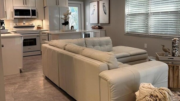 Una cucina moderna con mobili bianchi, forno integrato e microonde. Si nota un divano modulare beige e un cesto di vimini sul pavimento.