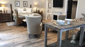 Quarto com cama, duas cadeiras, mesa com objetos decorativos, televisão e lareira.