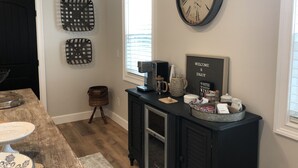 Uma cozinha com uma mesa de madeira, uma cafeteira, um relógio e uma placa de boas-vindas.