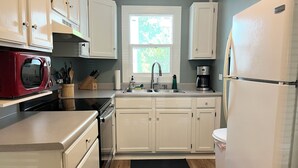A compact kitchen with white cabinets, a red microwave, a coffee maker, and a black rug on the floor.