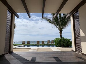 A wooden deck leading to a pool with lounge chairs and a view of the ocean. - Deluxe Beachfront Penthouse in Akumal (Akumal, Quintana Roo)