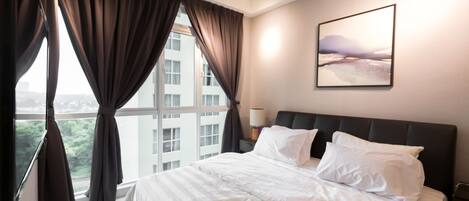 A hotel room with a large bed, a window with curtains, a bedside table with a lamp, and a framed picture on the wall.