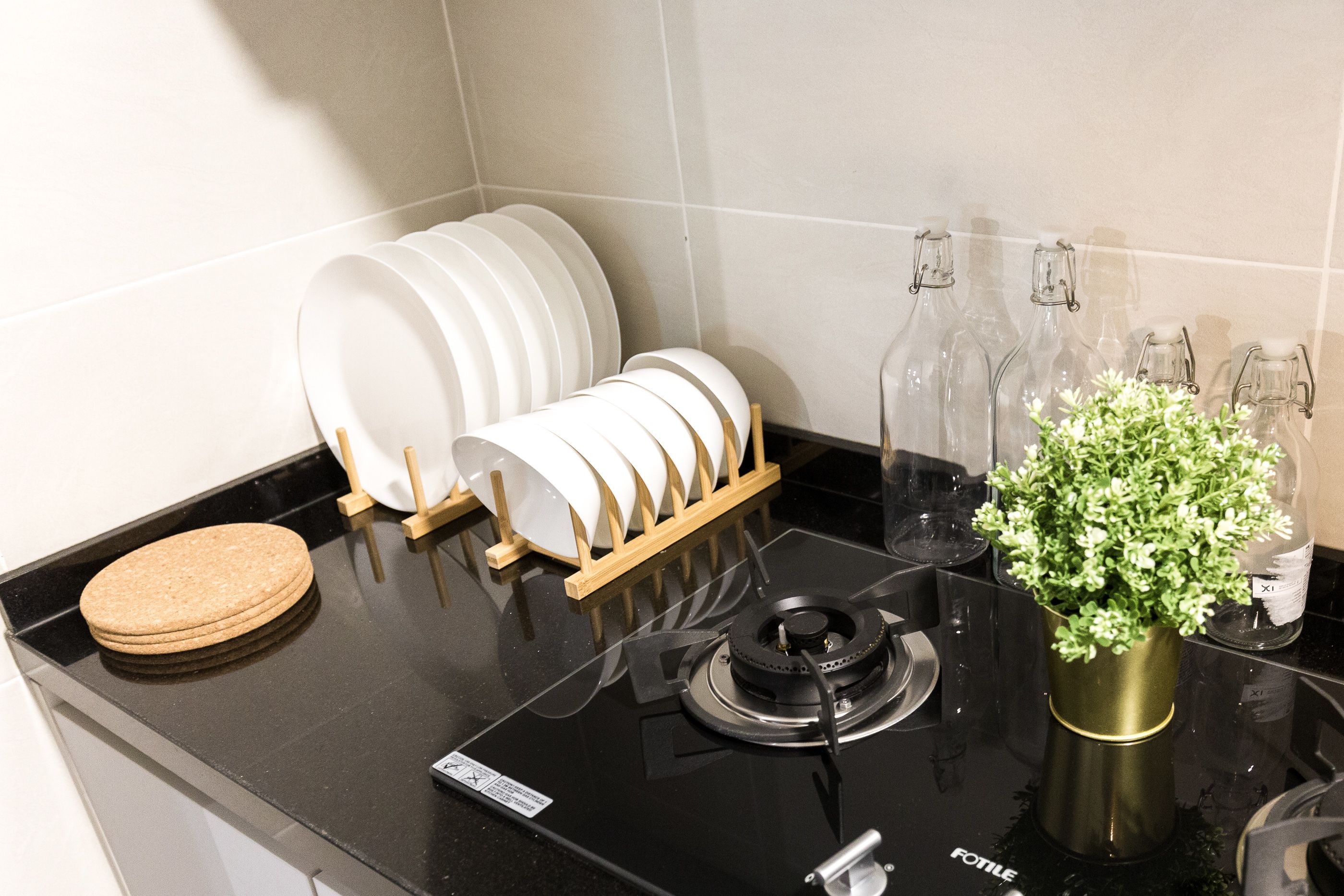 Una encimera de cocina con estufa a gas, escurreplatos, planta en maceta y varias botellas de vidrio.
