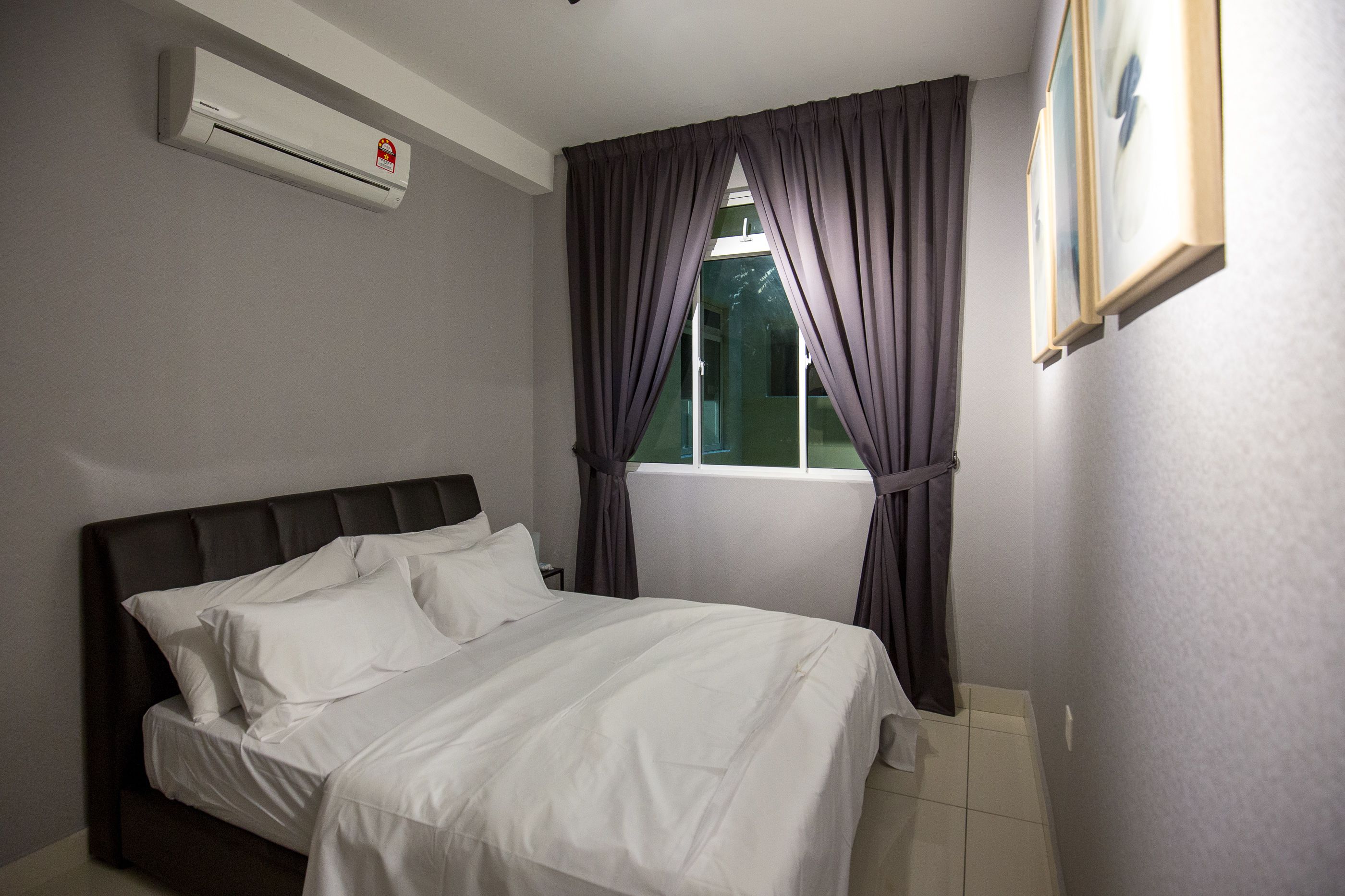 A bedroom with a bed, an air conditioner, a window with curtains, and a framed picture on the wall.