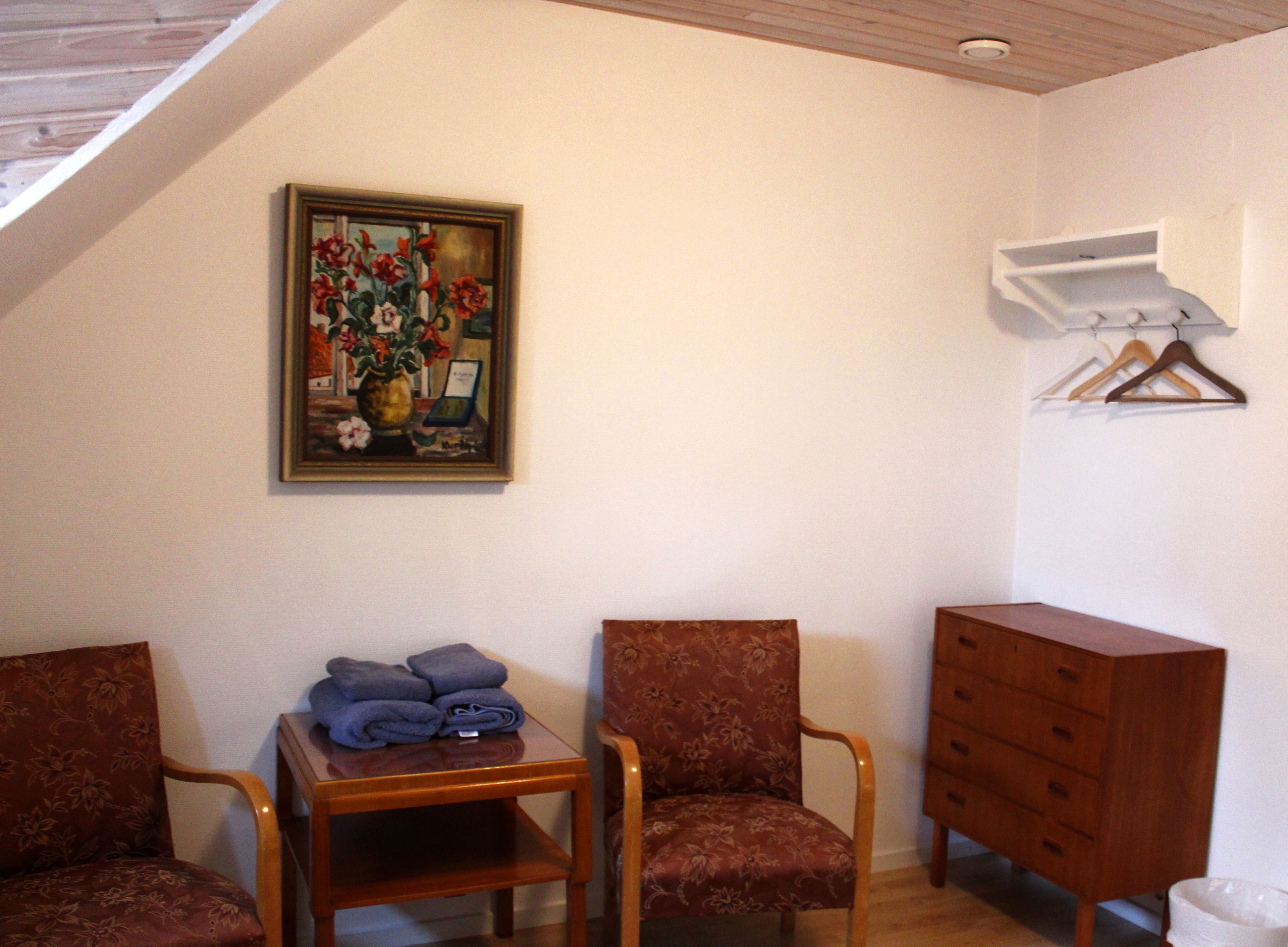Ein Zimmer mit zwei Stühlen, einem kleinen Tisch mit zusammengeklappten Handtüchern, einem Holzschrank, einem Blumenbild und einer weißen Klimaanlage.