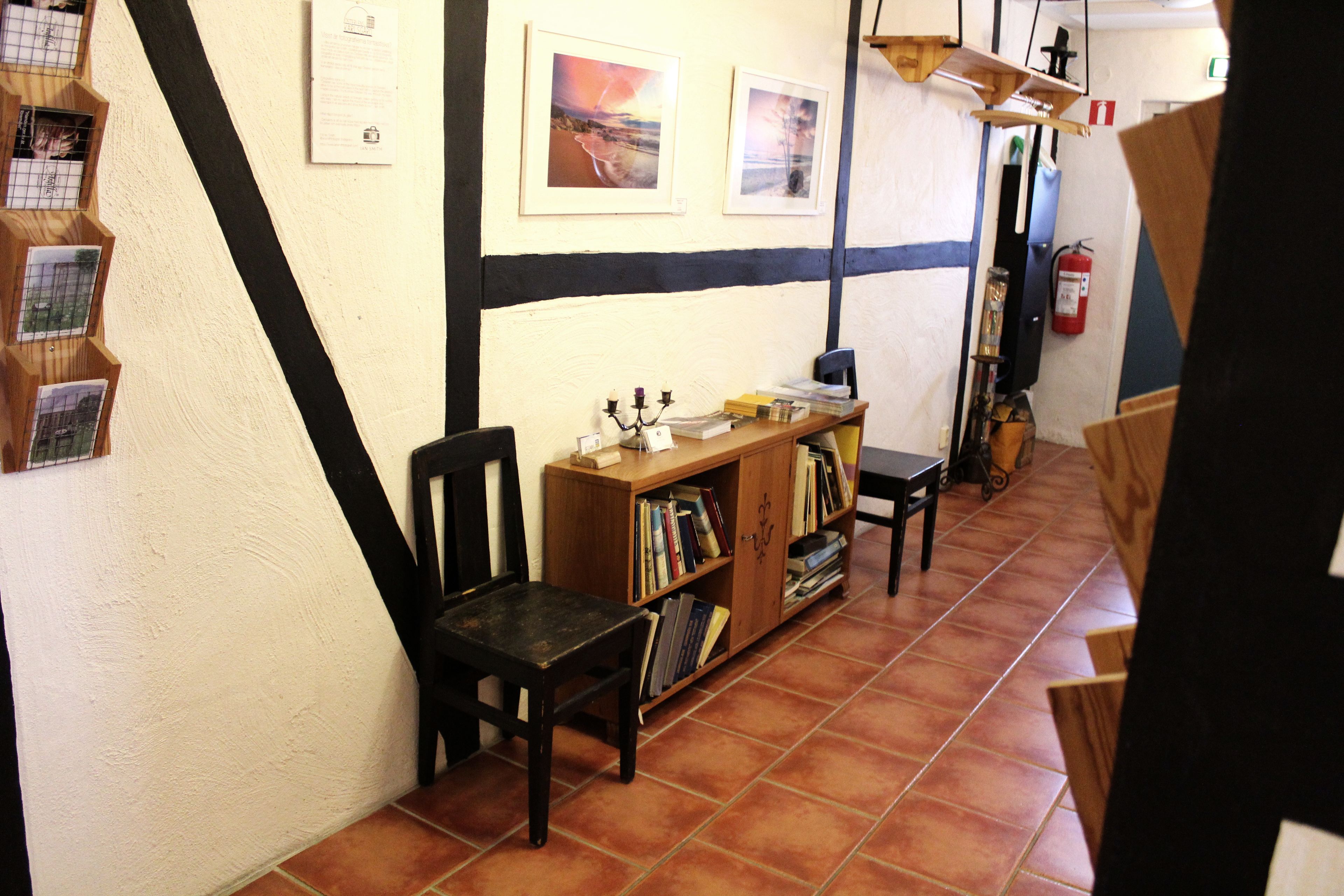 Un pasillo estrecho con una estantería de madera, una silla negra y un suelo de baldosas.