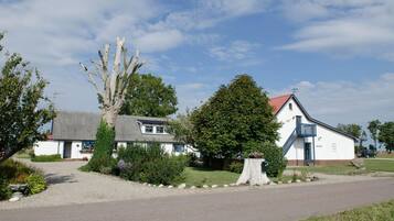 A rural setting with a white building with a red roof, a tree stump, and a gravel driveway.