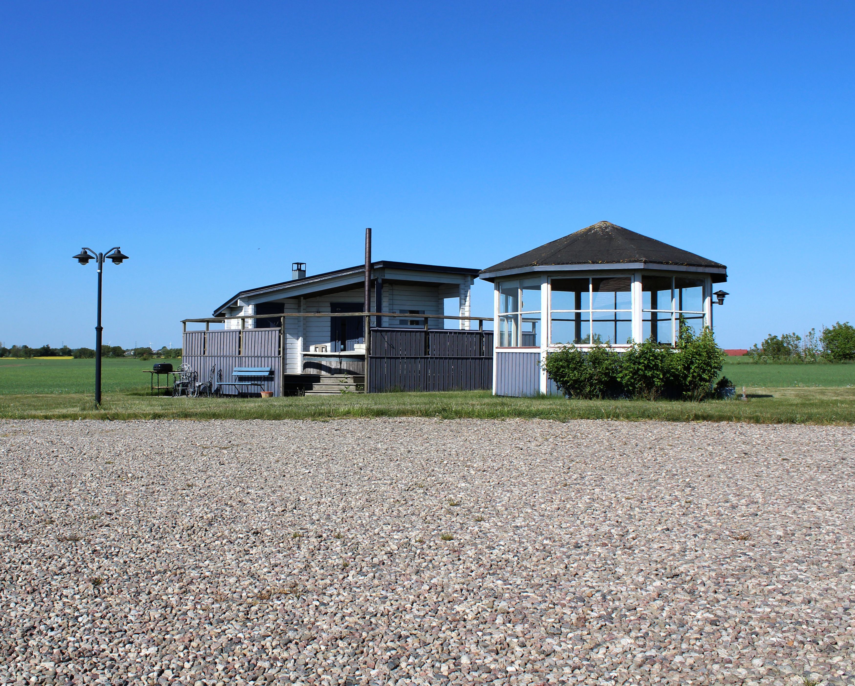 A building with a large open porch, a separate glass structure, and a gravel driveway.