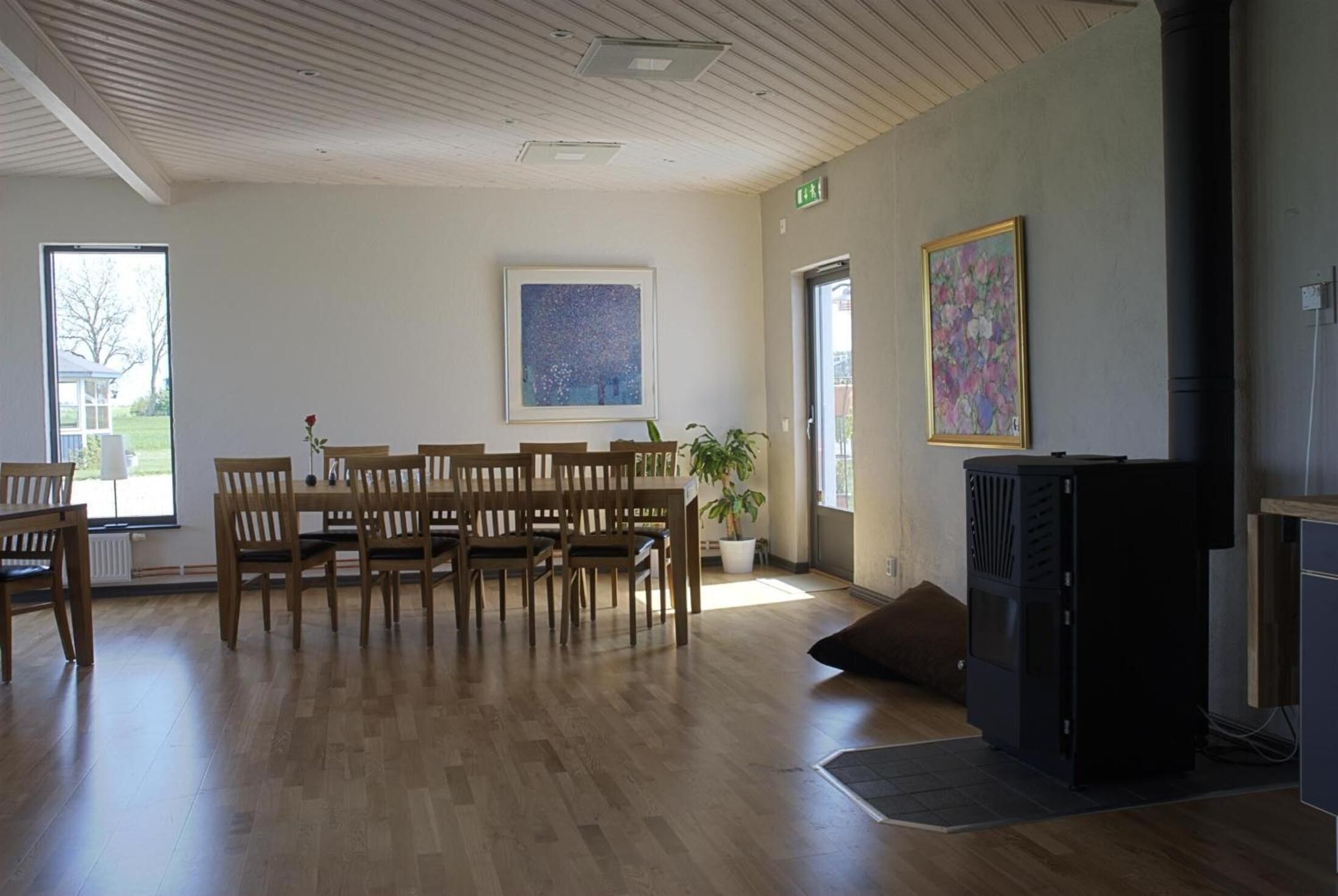 Une pièce spacieuse avec une table et des chaises en bois, une grande fenêtre, une plante en pot et un haut-parleur noir.
