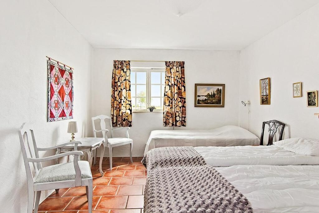 A room with two beds, a chair, a table, and curtains.