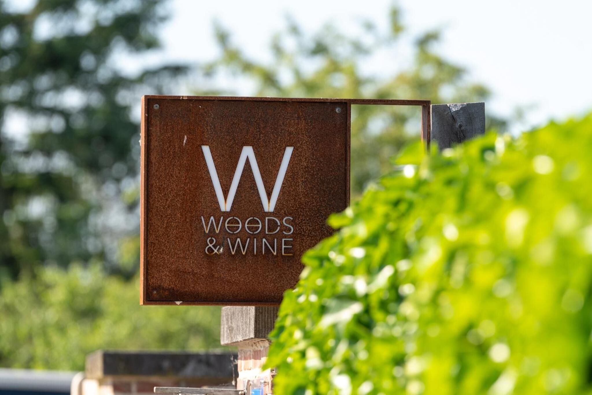 A sign with the text "Woods & Wine" mounted on a metal structure.