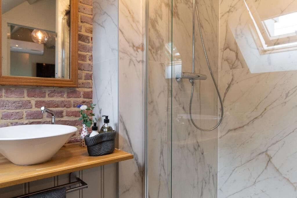 A bathroom with a large white sink, a mirror, a shower enclosure, and a wooden countertop.