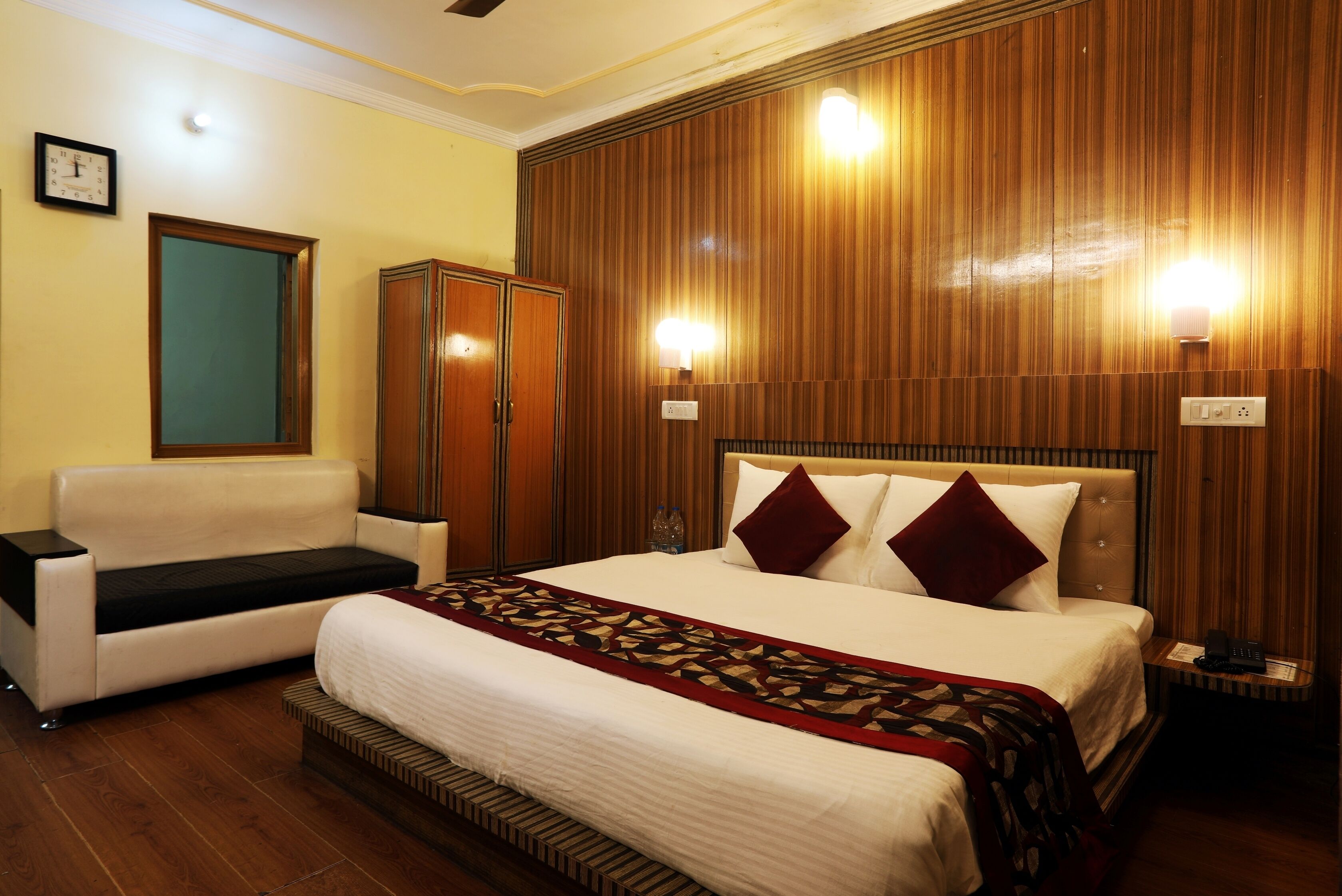 Una habitación de hotel con cama, sofá, armario y dos luces empotradas.