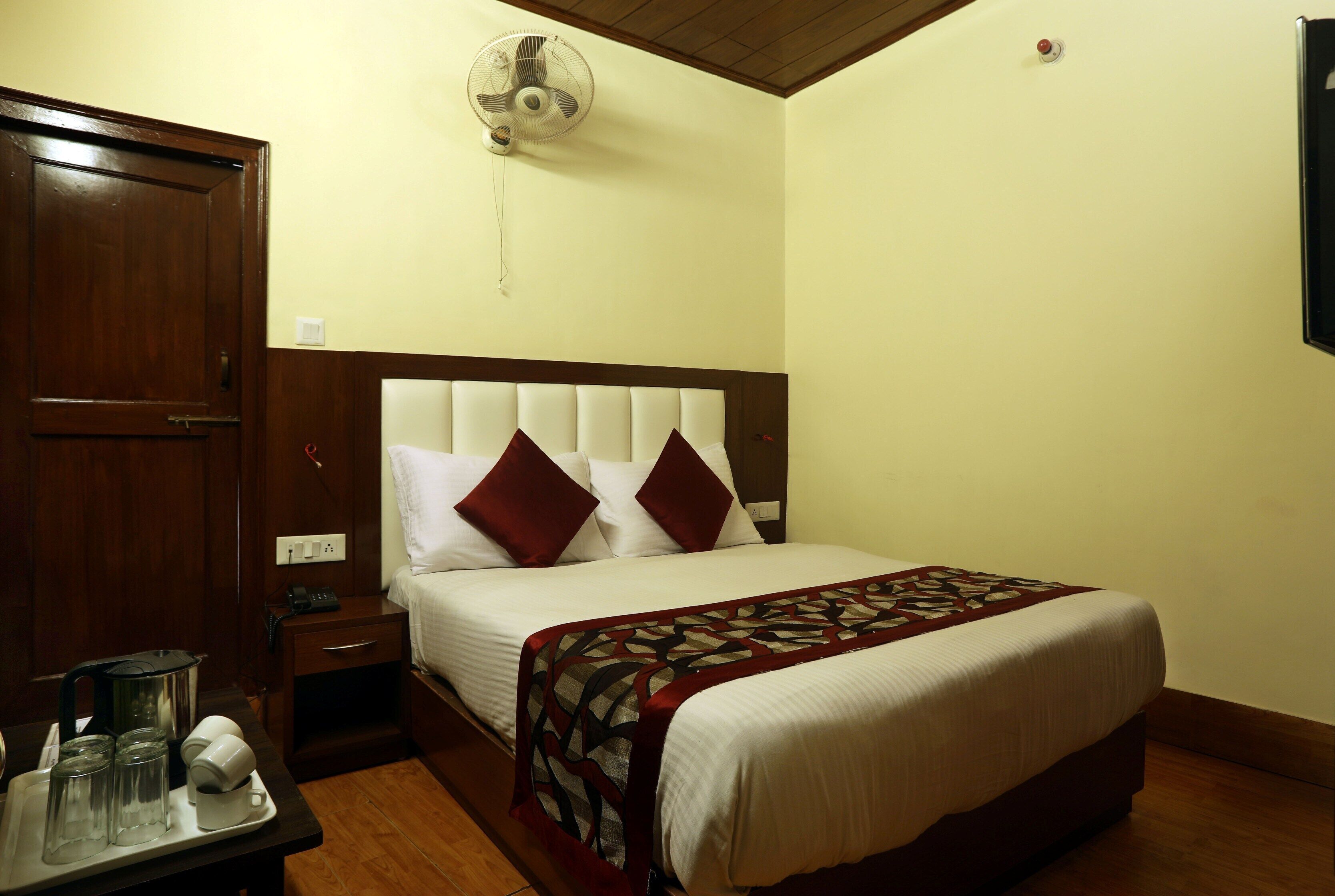 Una habitación de hotel con cama, mesita de noche y ventilador.