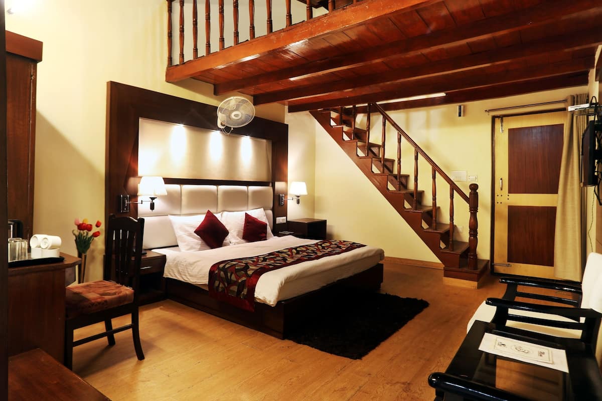 A bedroom with a wooden bed, a desk, a chair, a nightstand, a fan, a staircase, and a door.