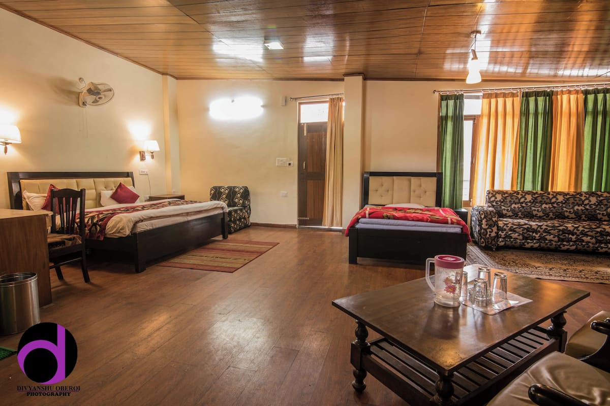 A hotel room with a bed, a sofa, a table with a pitcher and glasses, and a wooden floor.