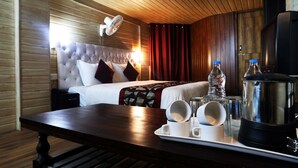 Habitación de hotel con techo de madera, cama con cabecera capitonada, mesita de noche con bandeja de desayuno y un televisor.