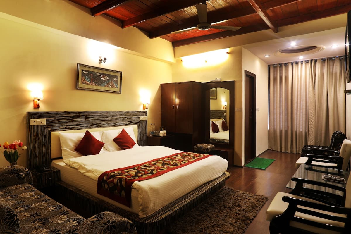 A hotel room with a large bed, a wooden headboard, a nightstand, a mirror, a desk with chairs, and a green mat on the floor.