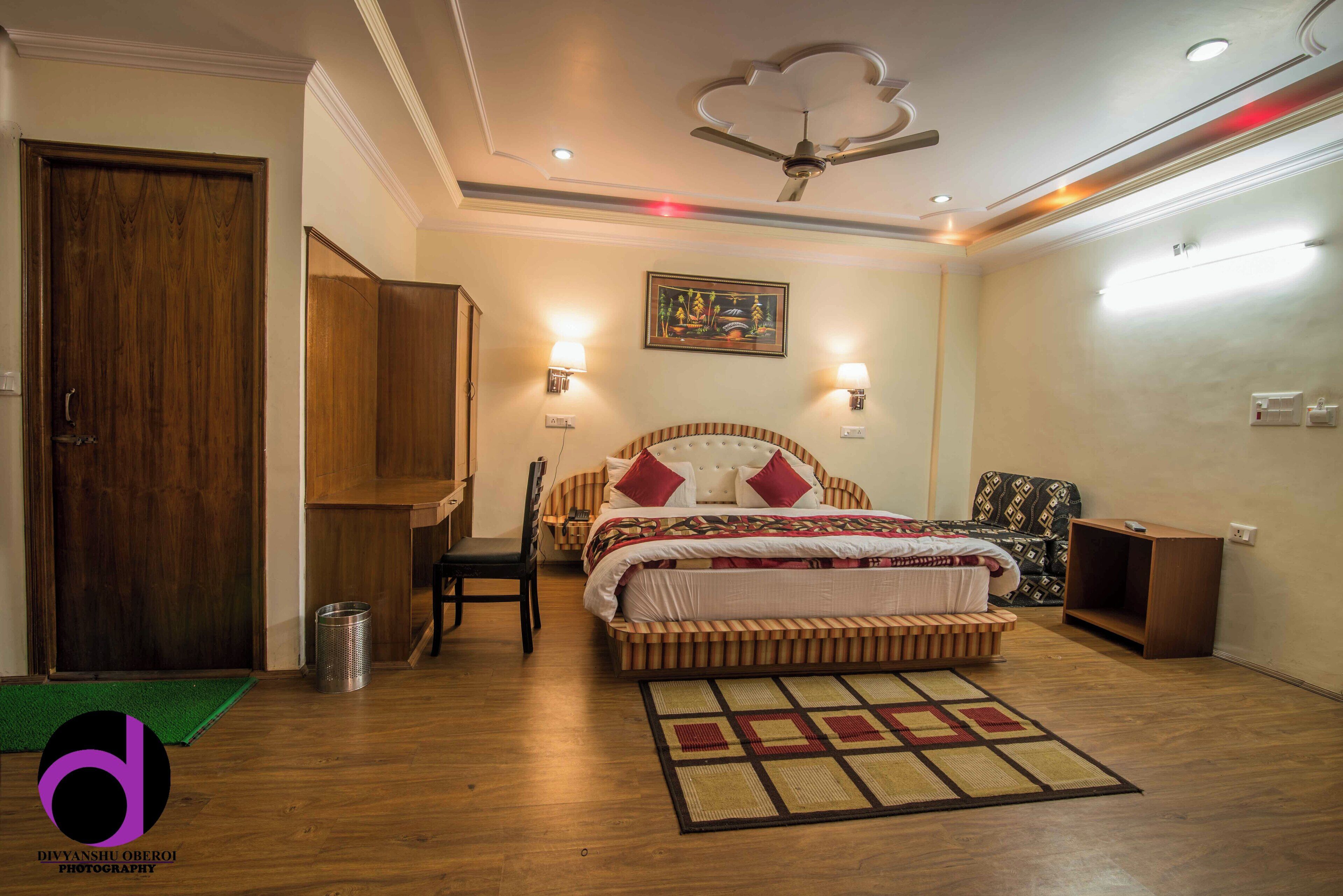 A bedroom with a bed, a desk, a chair, a ceiling fan, and a wall-mounted light fixture.