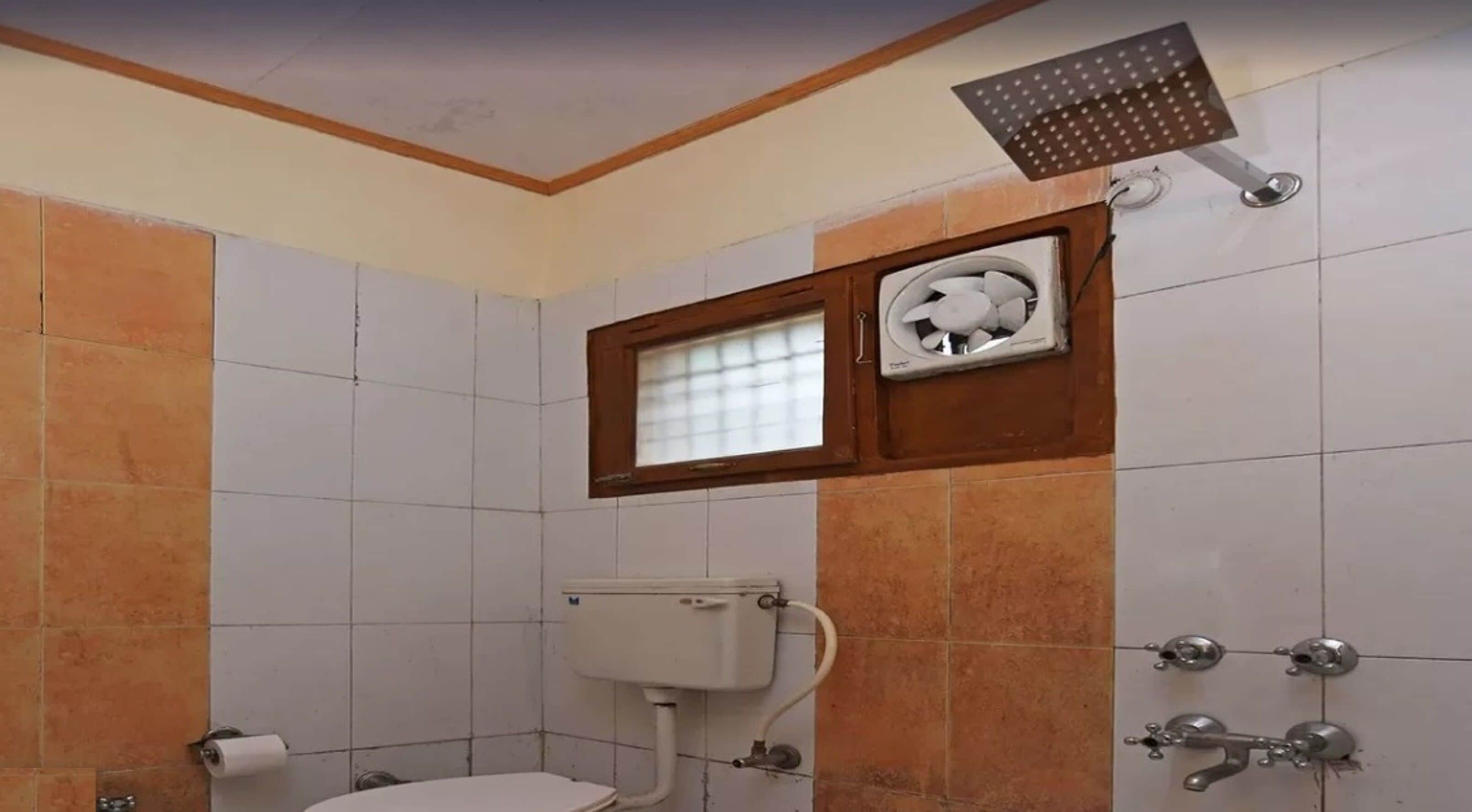 Un baño con inodoro, ventana, ducha y dispensador de papel higiénico.