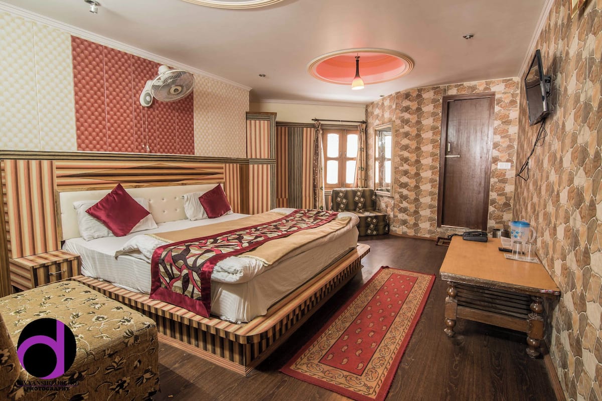 A bedroom with a large bed, a wooden nightstand, a small table, and a red rug.