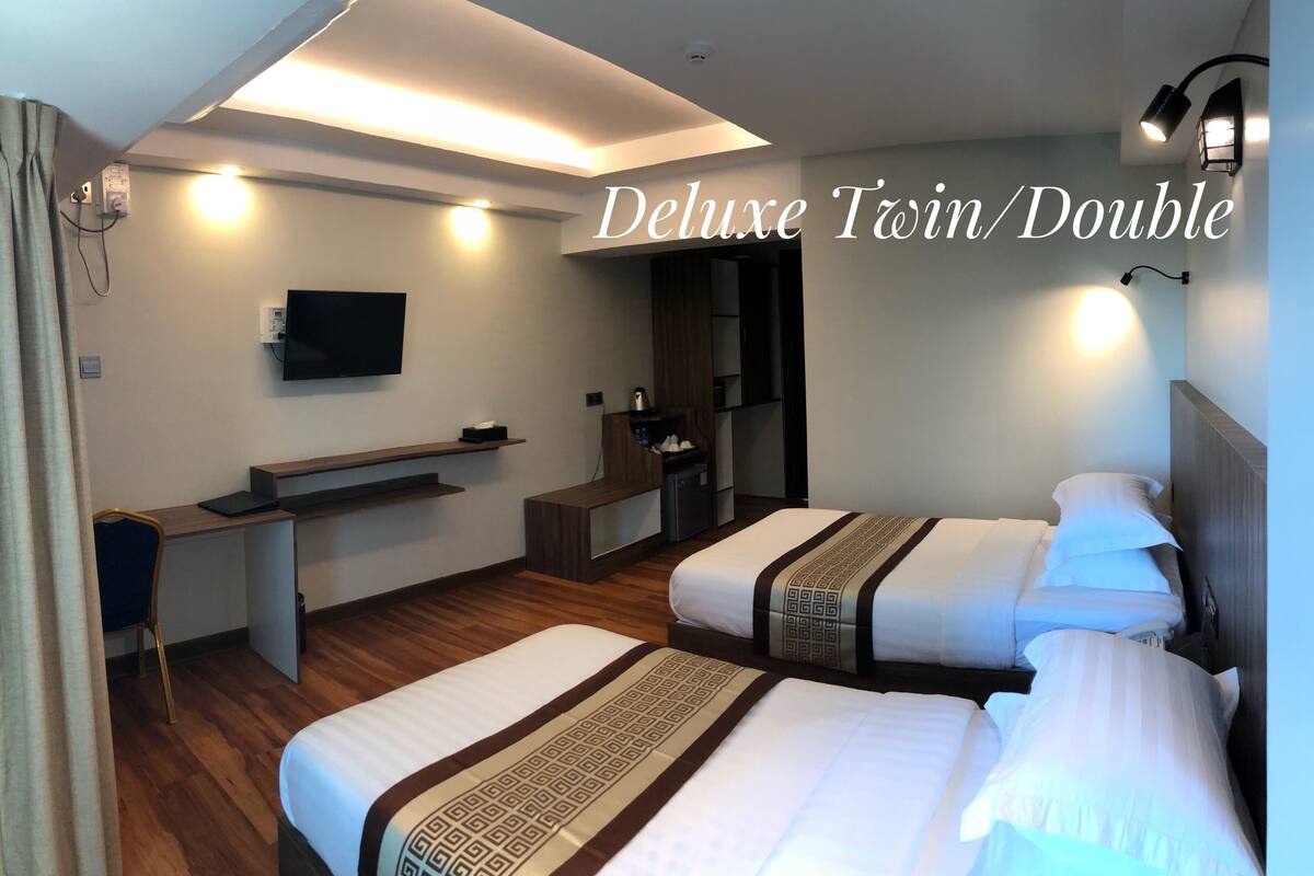 A Deluxe Twin/Double room with two beds, a desk, a TV, and a minibar.