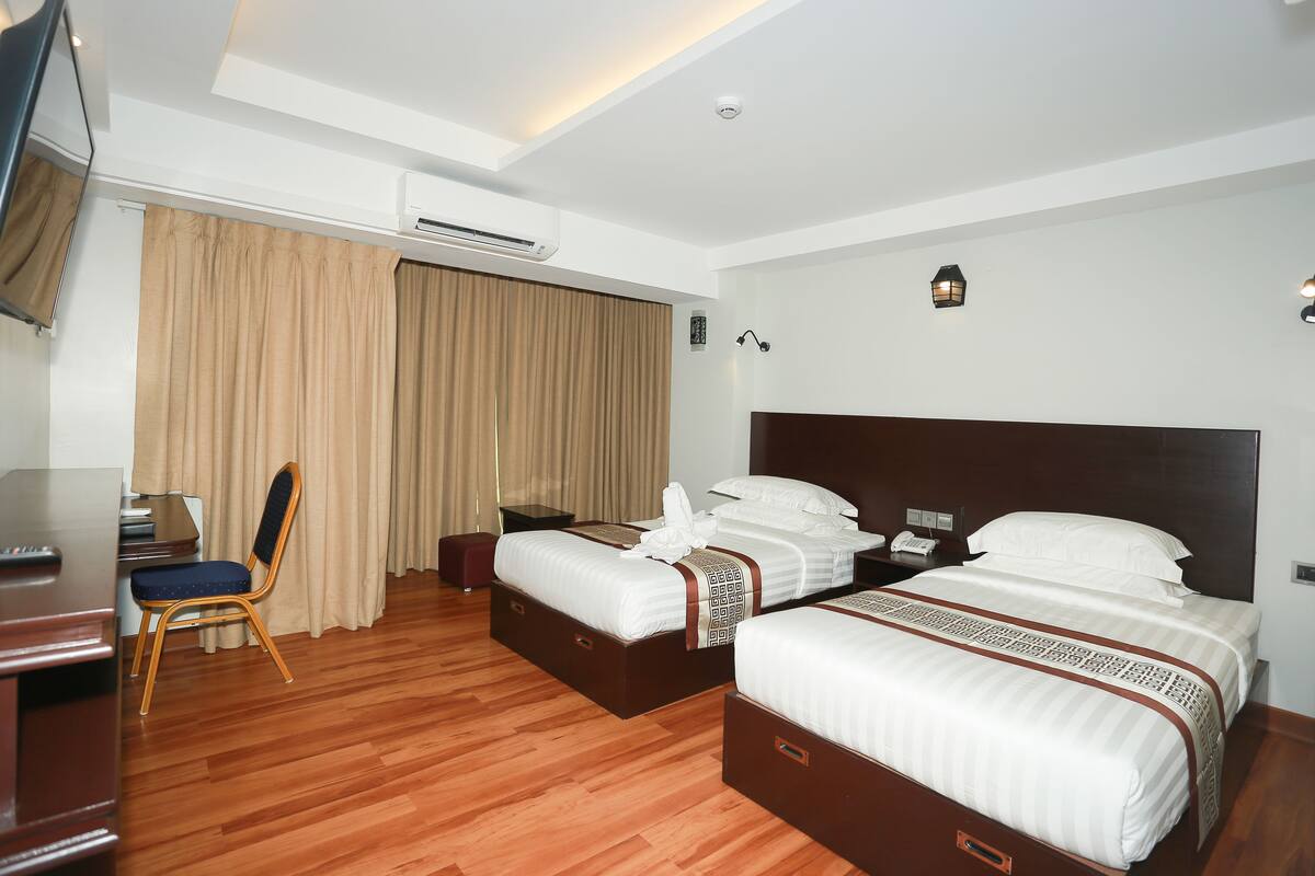 A hotel room with two beds, a desk, a chair, and a TV.